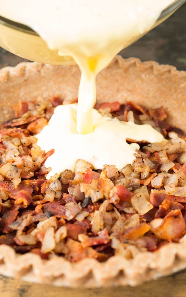 The duck egg mixture being poured over the bacon and shallots in the quiche crust.