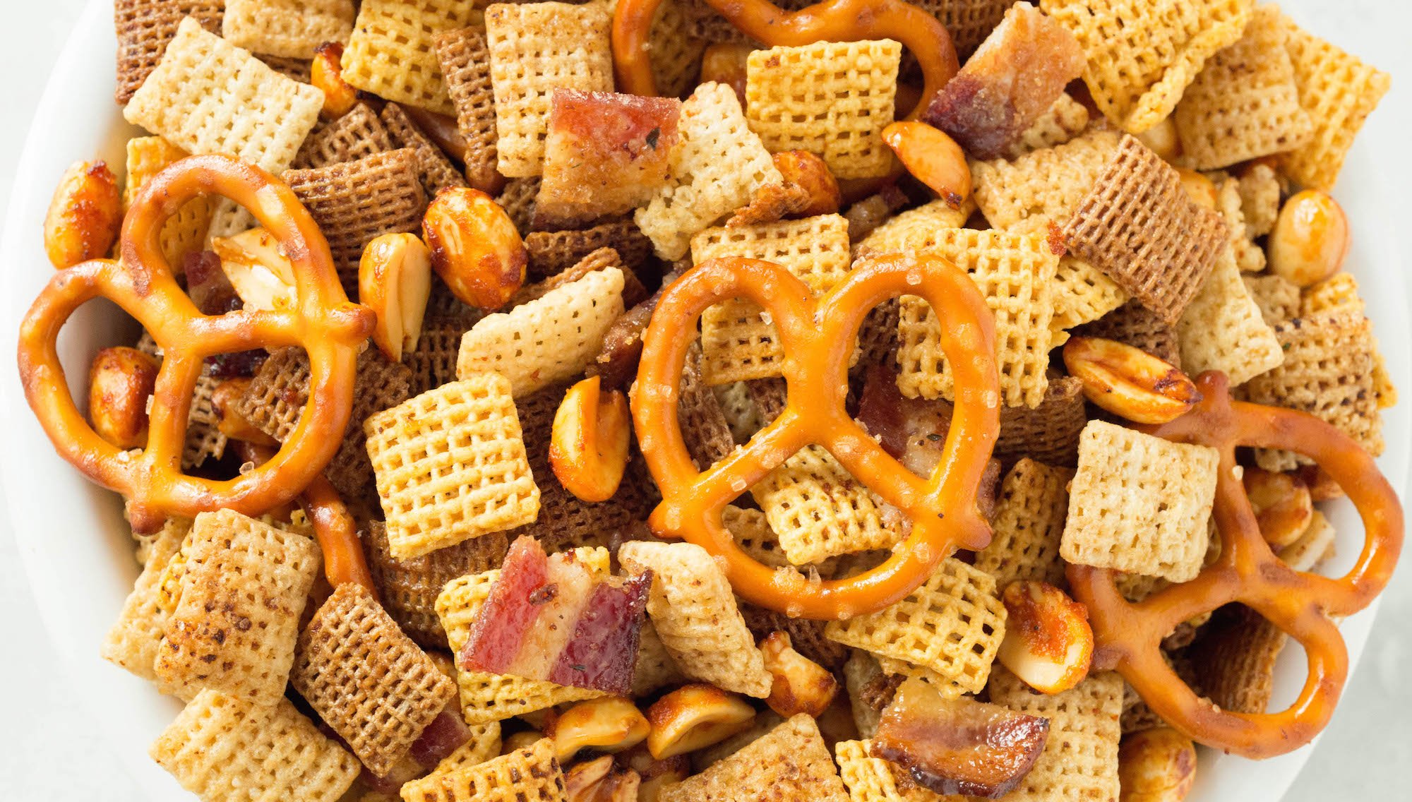 Overhead close up of duck fat Chex mix with white and wheat Chex squares, mini pretzels, chopped bacon, and seasoned peanuts.