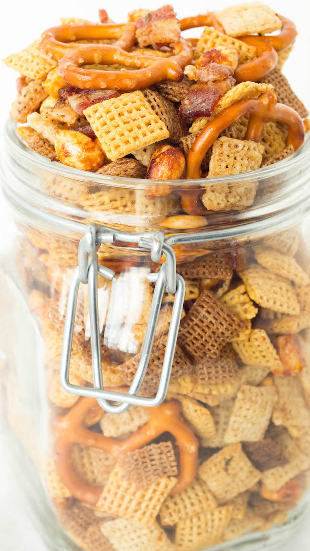 A glass jar with a hinged lid is overflowing with duck fat Chex mix.