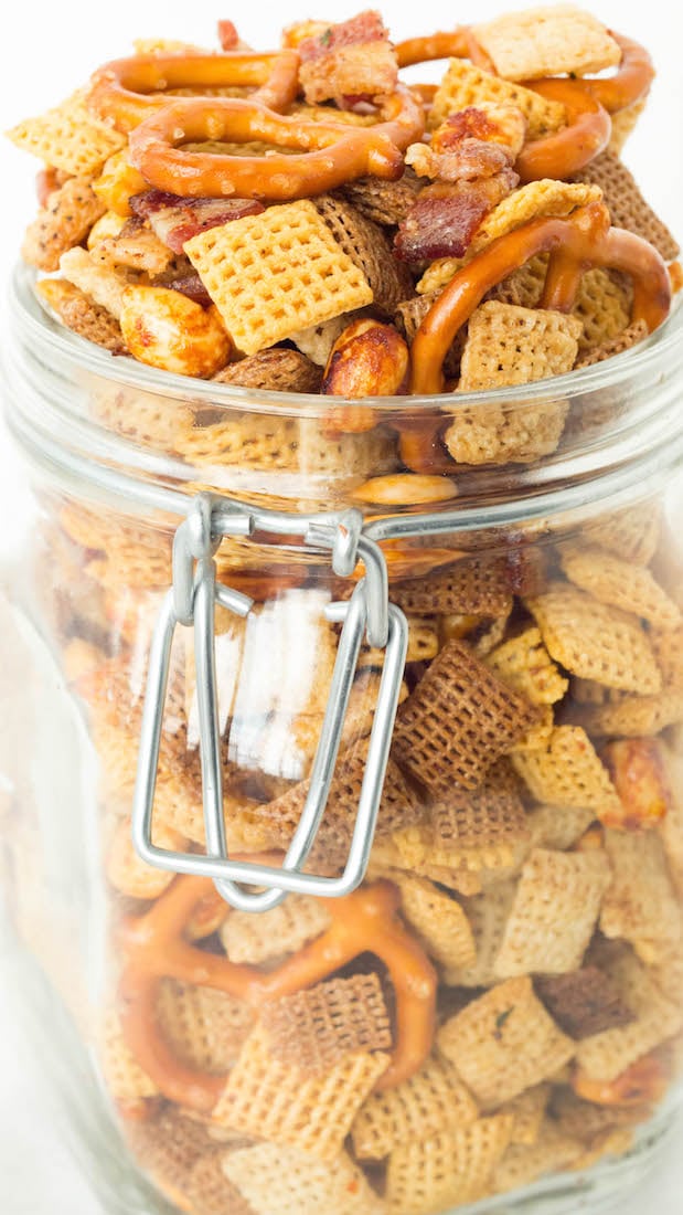 A glass jar with a hinged lid is overflowing with duck fat Chex mix.