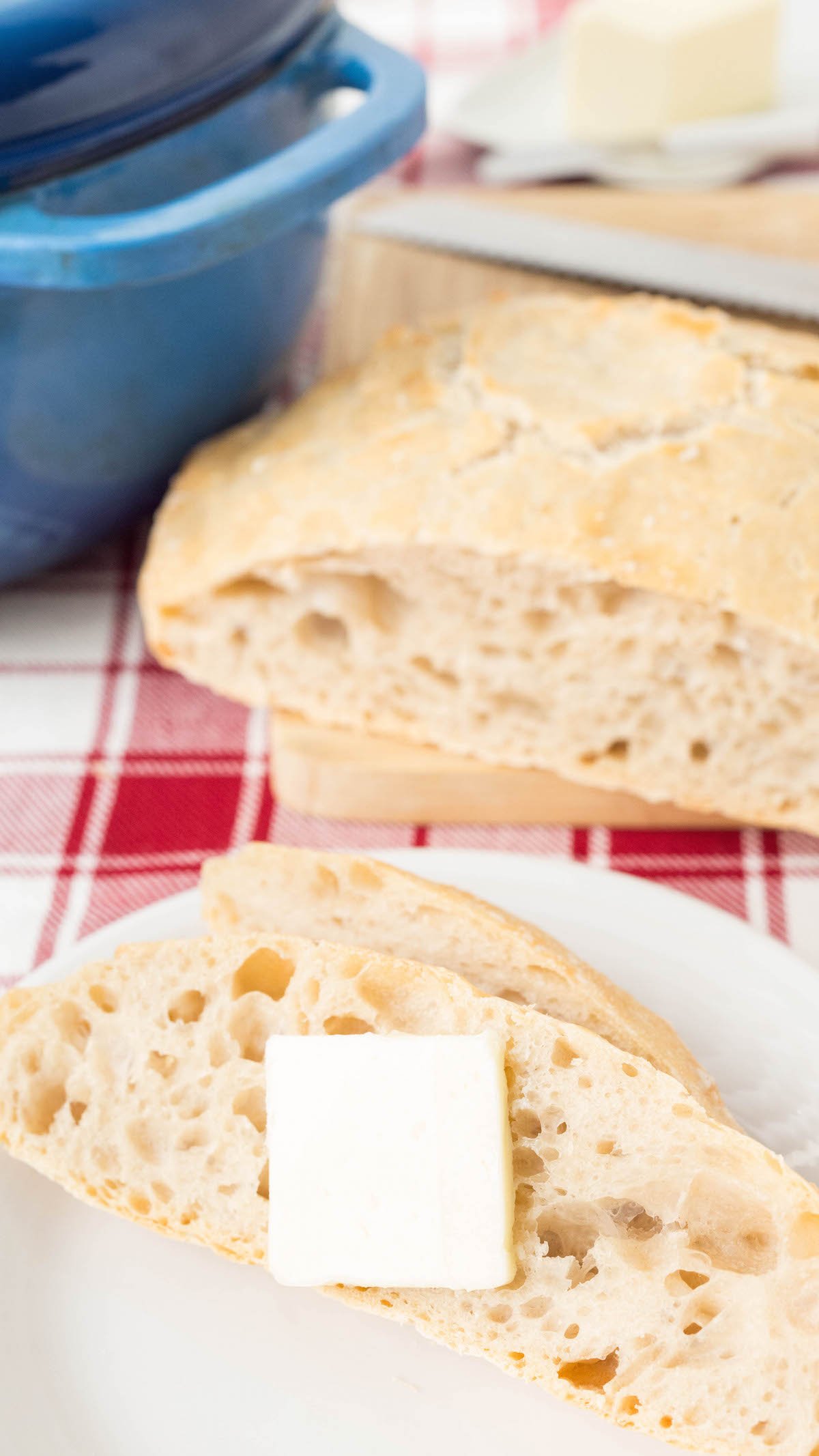 Close up of two slices of easy no knead dutch oven bread on a small white serving plate in front of the rest of the uncut loaf.