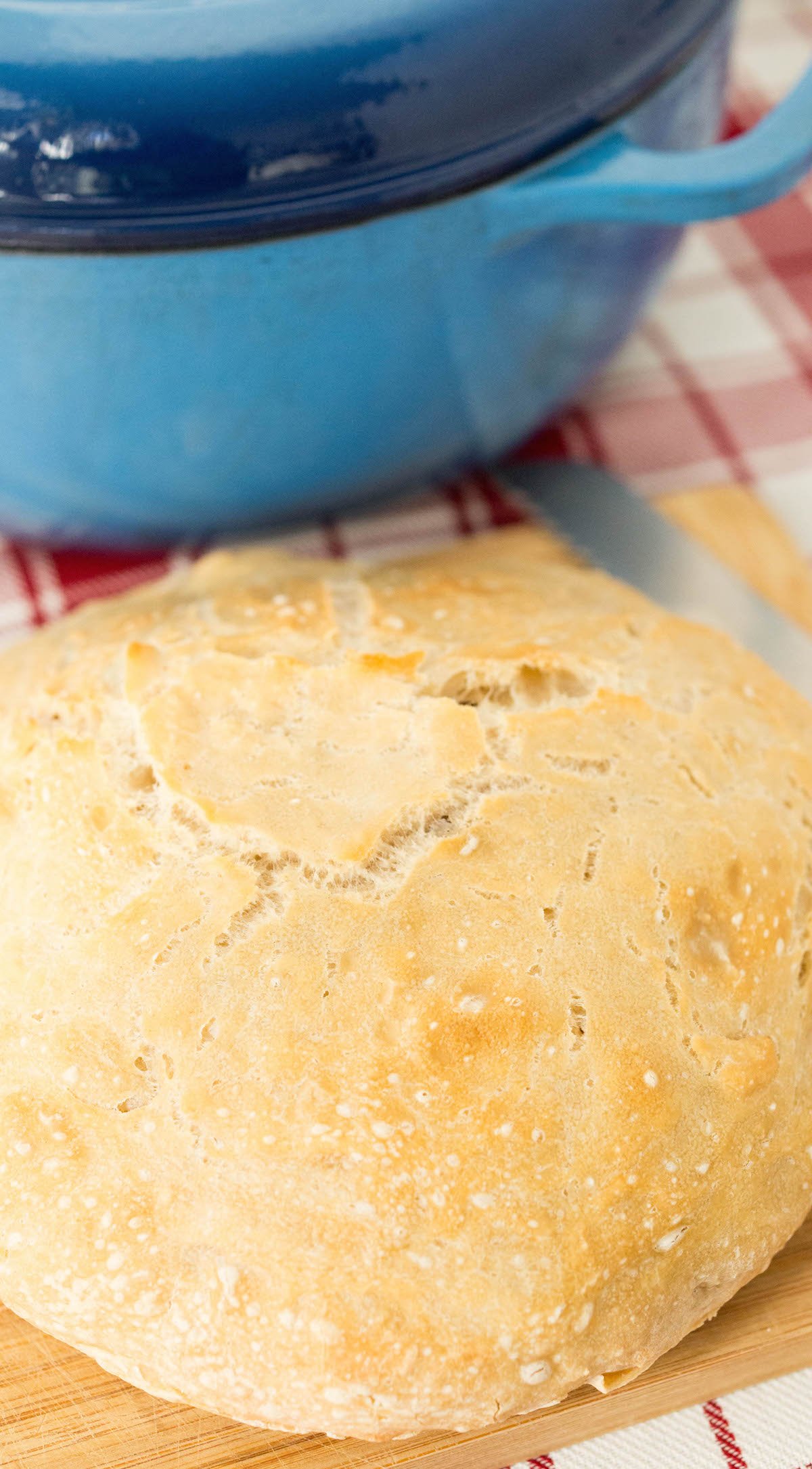 A white circular loaf of easy dutch oven bread sits on a cutting board in front of the pot.