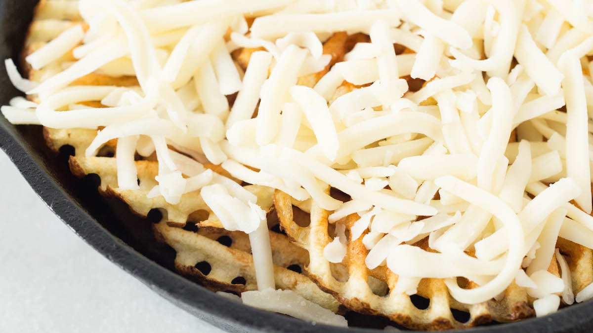 A cast iron skillet has been filled with waffle fries on the bottom, then topped with mozzarella cheese.
