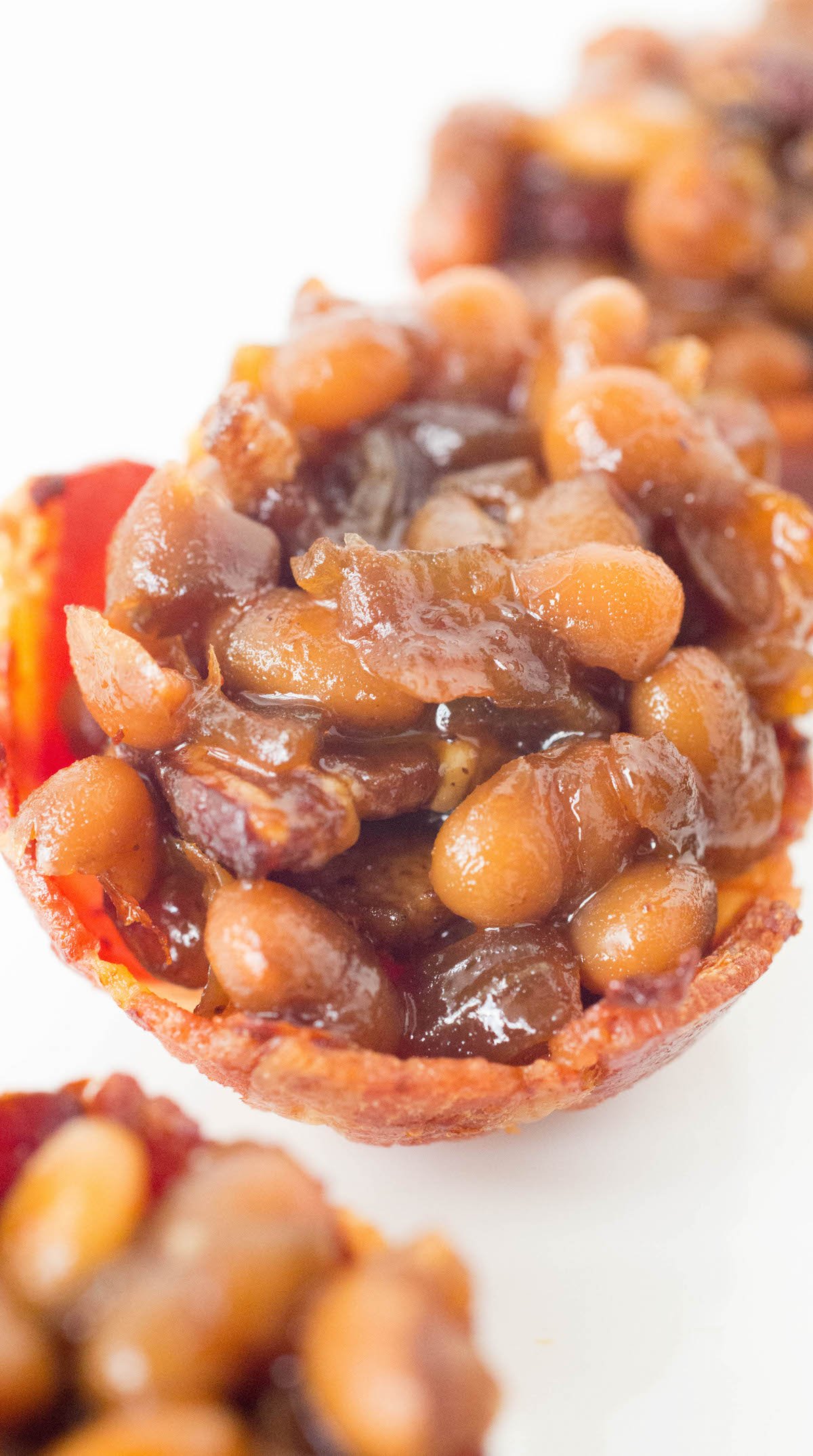 Homemade baked beans are sitting in miniature cups made out of bacon.