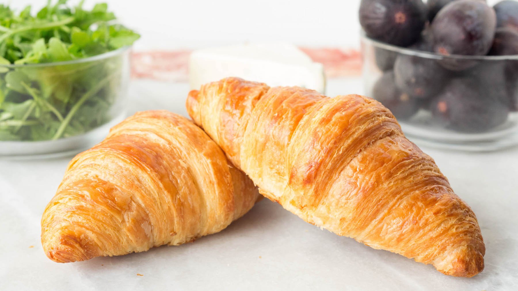 All the ingredients to make a fig croissant sandwich - fresh croissants, arugula, prosciutto, blue cheese, and fresh figs.