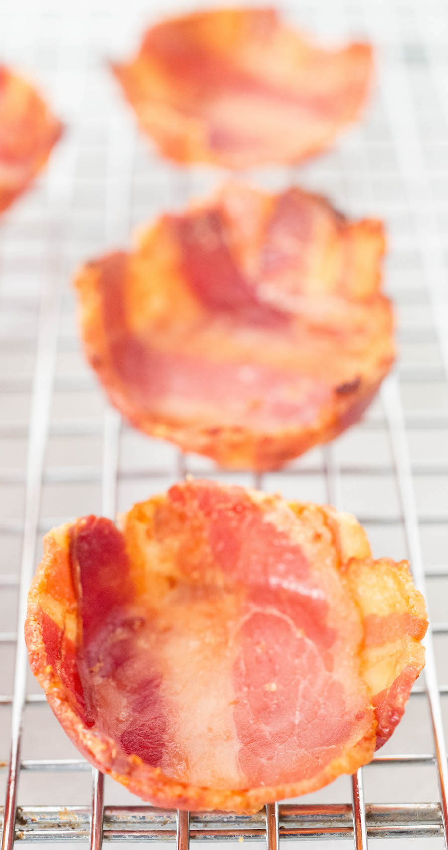 Mini bacon cups to serve baked beans in sitting on a wire metal rack.