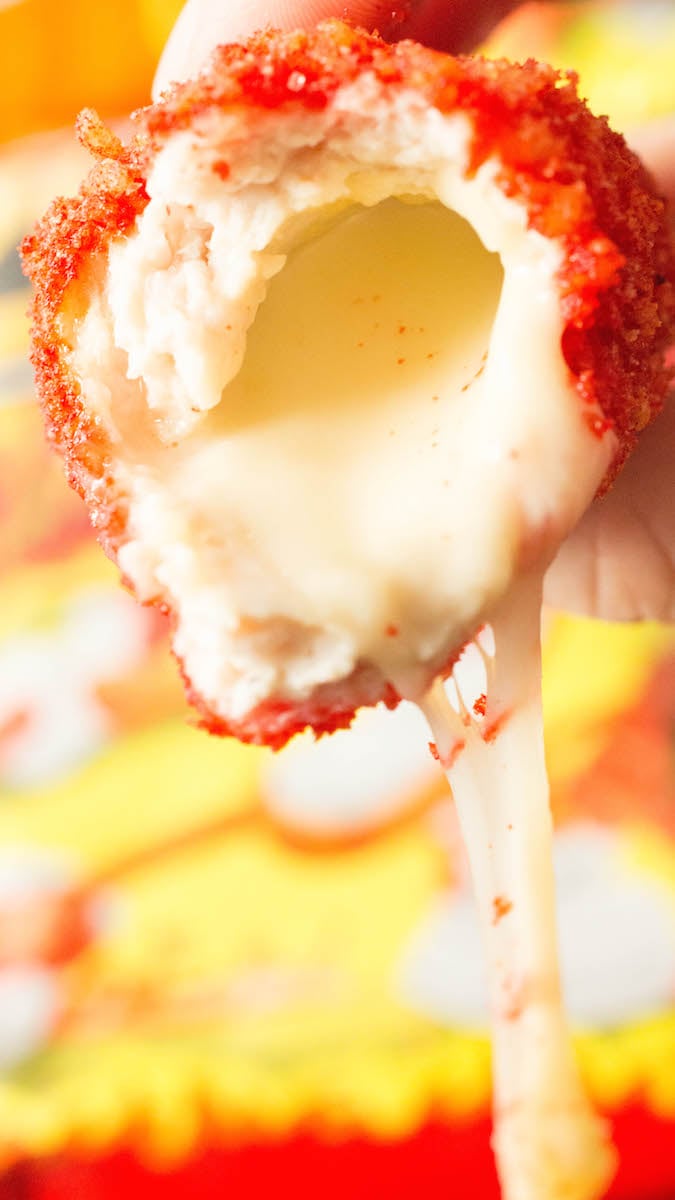 A close up of a flaming hot Cheetos cheese stick with a bite taken out of it. Cheese is dripping out of the bottom.