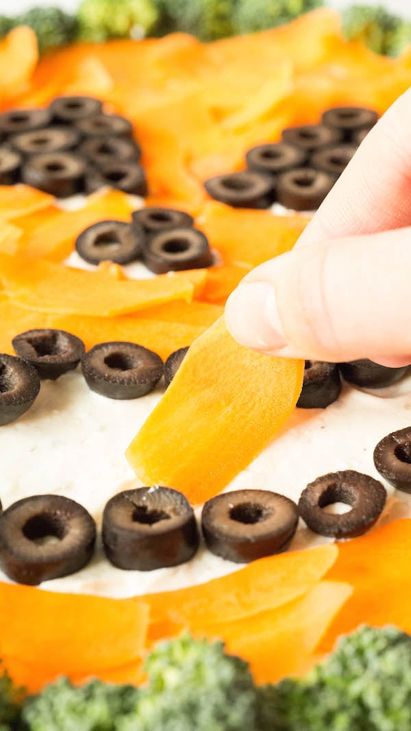 Placing shaved carrots on the Jack o' lantern Halloween pizza.