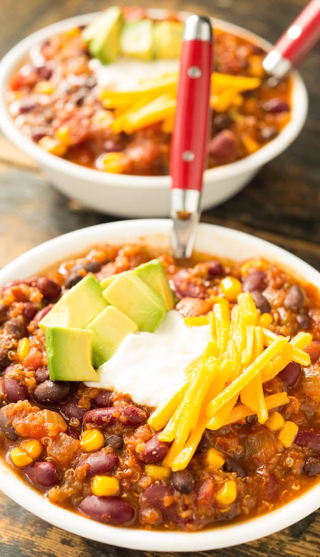 Close up of a bowl of meatless quinoa chilli topped with sour cream, avocado, and shredded cheddar cheese