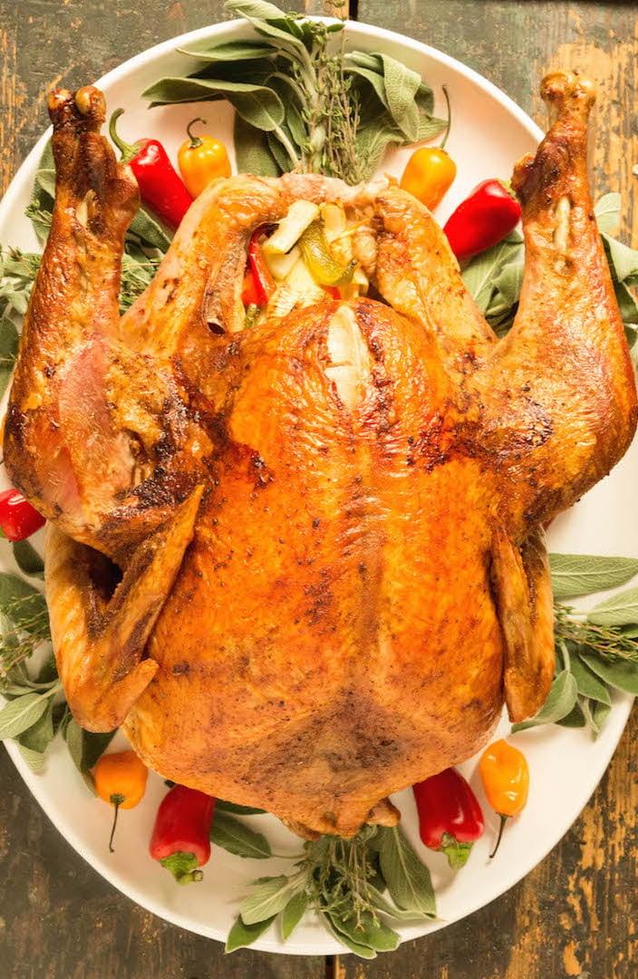 Overhead view of a cajun turkey on a white platter. It's garnished with fresh herbs and spicy peppers.