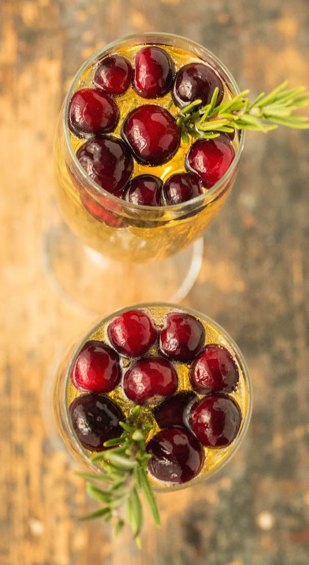 Two champagne flutes filled with white grape mimosas, topped with fresh cranberries and a sprig of rosemary.