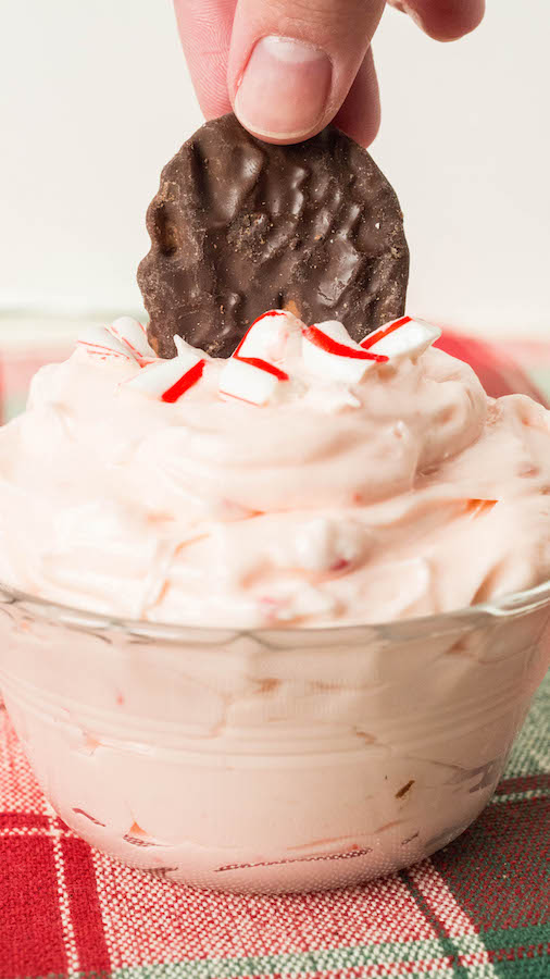 A finger dips a chocolate potato chip into Peppermint Fluff Christmas Dip.