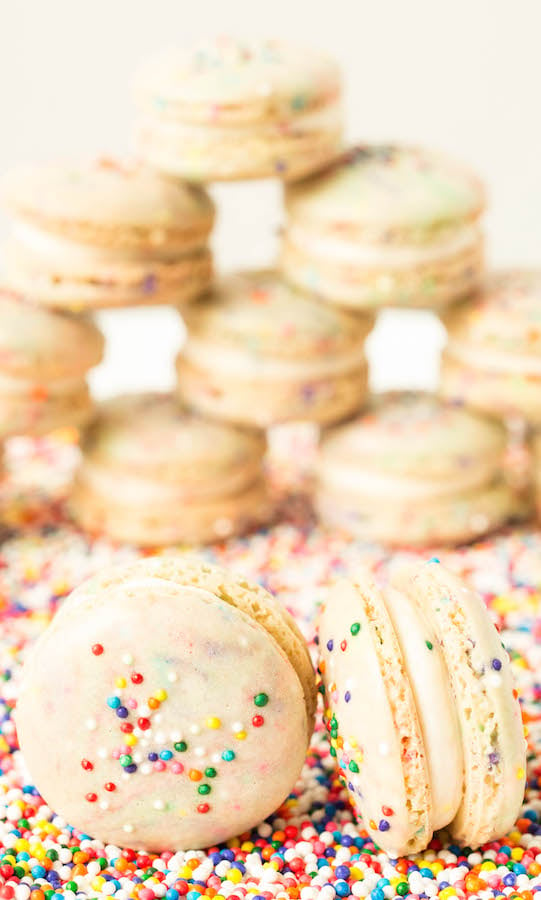 Two funfetti birthday macaroons are in focus in the foreground, a pyramid of them is out of focus in the background.