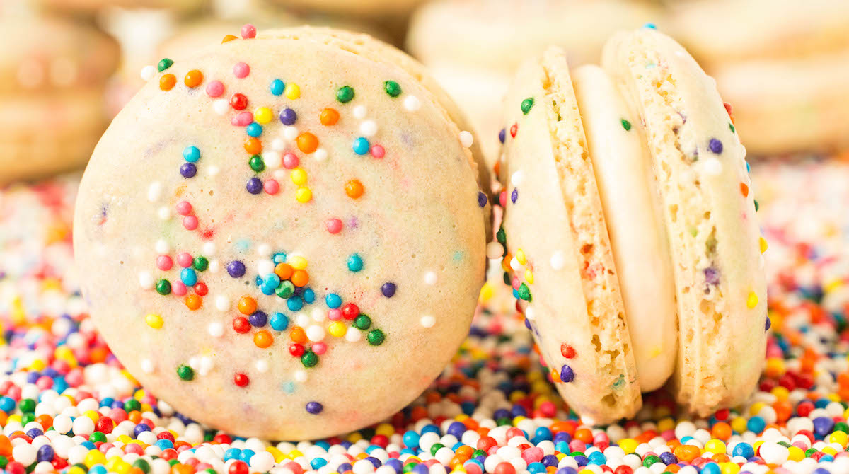 Close up of two Funfetti Birthday Macaroons sitting on top of sprinkles.