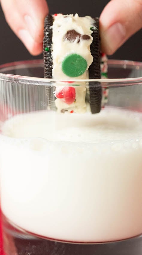 Close up of a hand dipping a Christmas Cookie Dough Stuffed Oreo into a glass of milk.