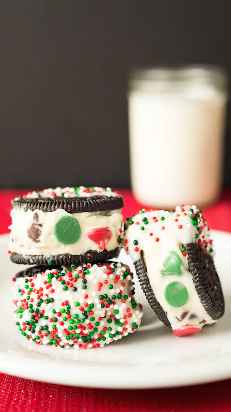 Oreo cookies stuffed with Christmas cookie dough then dipped in white chocolate sitting in front of a glass of milk.