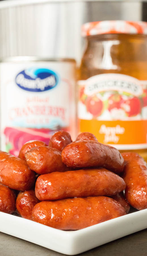 Close up of apple cranberry lil' smokies sitting in front of apple jelly and cranberry sauce.