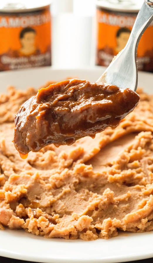 A fork holds up adobo peppers in front of a plate of refried beans.