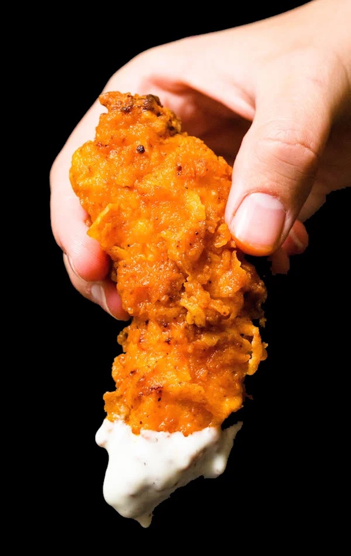 A hand holds up a breaded and fried chicken tender that's been completely coated in an orange buffalo sauce and the tip has been dipped in ranch dressing.