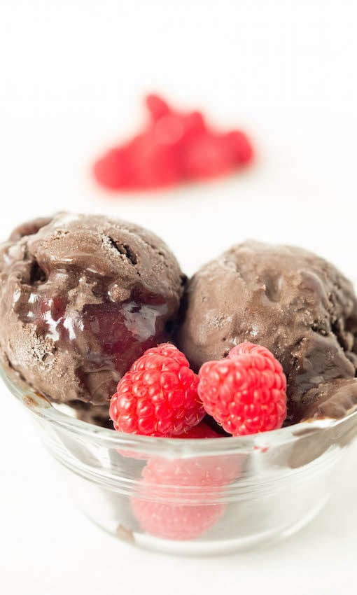 Two scoops of dark chocolate raspberry gelato in a clear bowl on a white background.