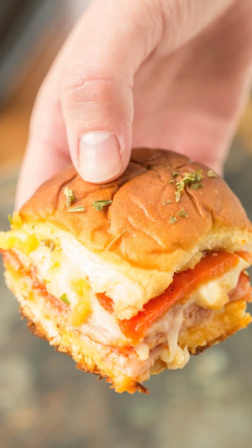 A hand holds up a single Hawaiian Roll Italian Slider.