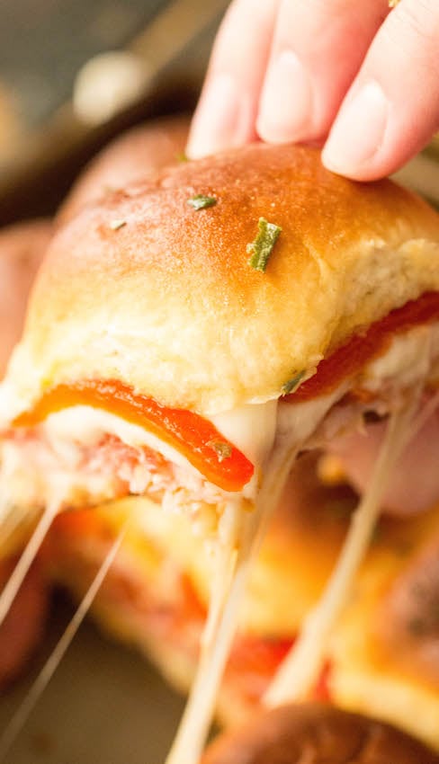 A hand picking up a Hawaiian Roll Italian Slider as cheese oozes out.