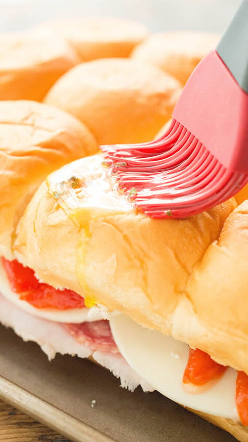 Brushing butter & herbs on Italian Hawaiian Roll Sliders before baking.