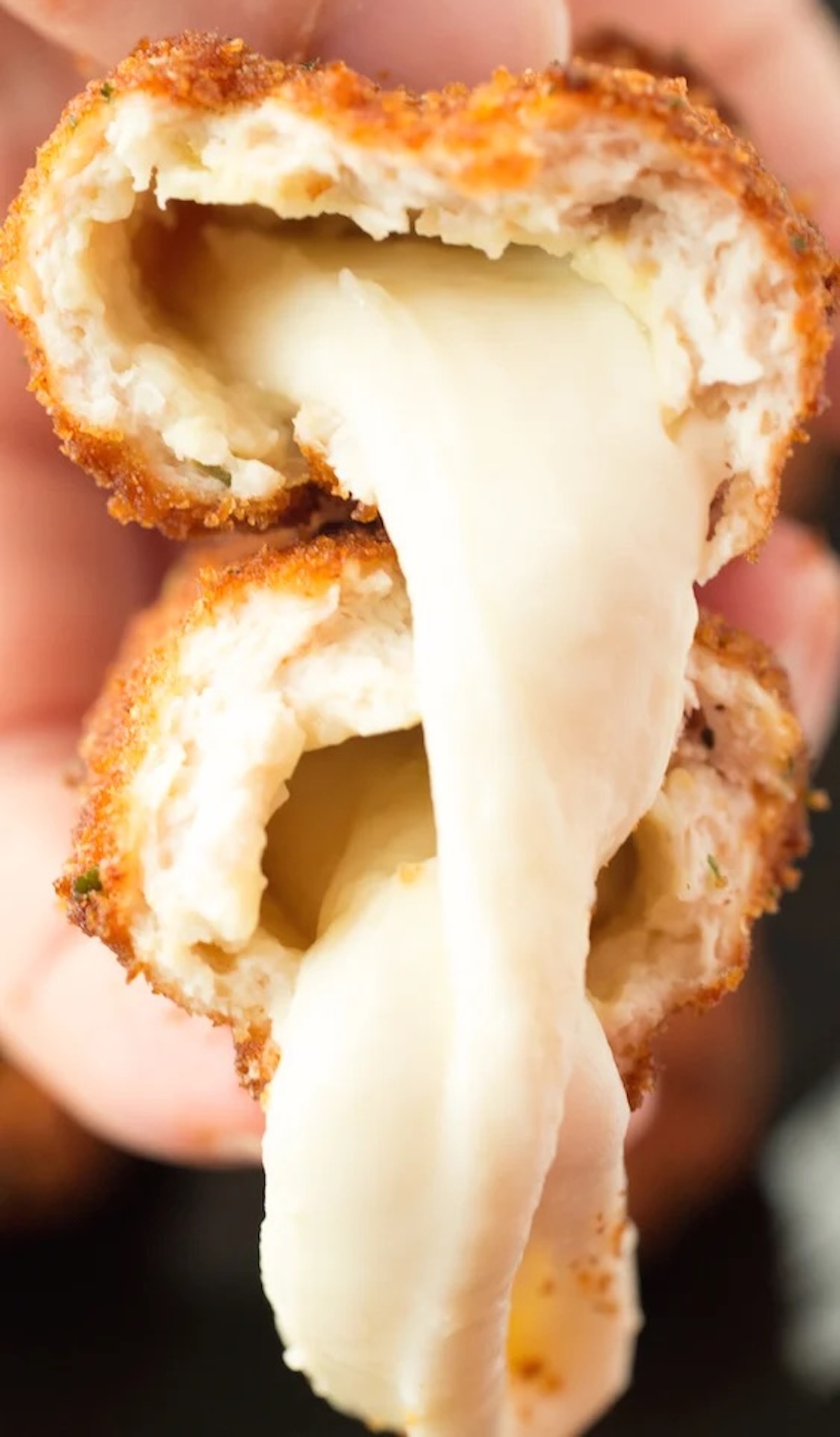 Fingers hold up a mozzarella stick that's been split in half to show the cheese oozing out.