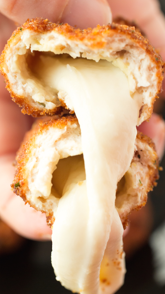A mozzarella stick coated in chicken and breading thats been fried, then sliced in half to show the melted cheese oozing out.