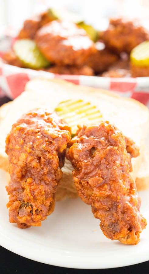 Two Nashville Hot fried chicken wings next to a slice of white bread and a pickle slice.