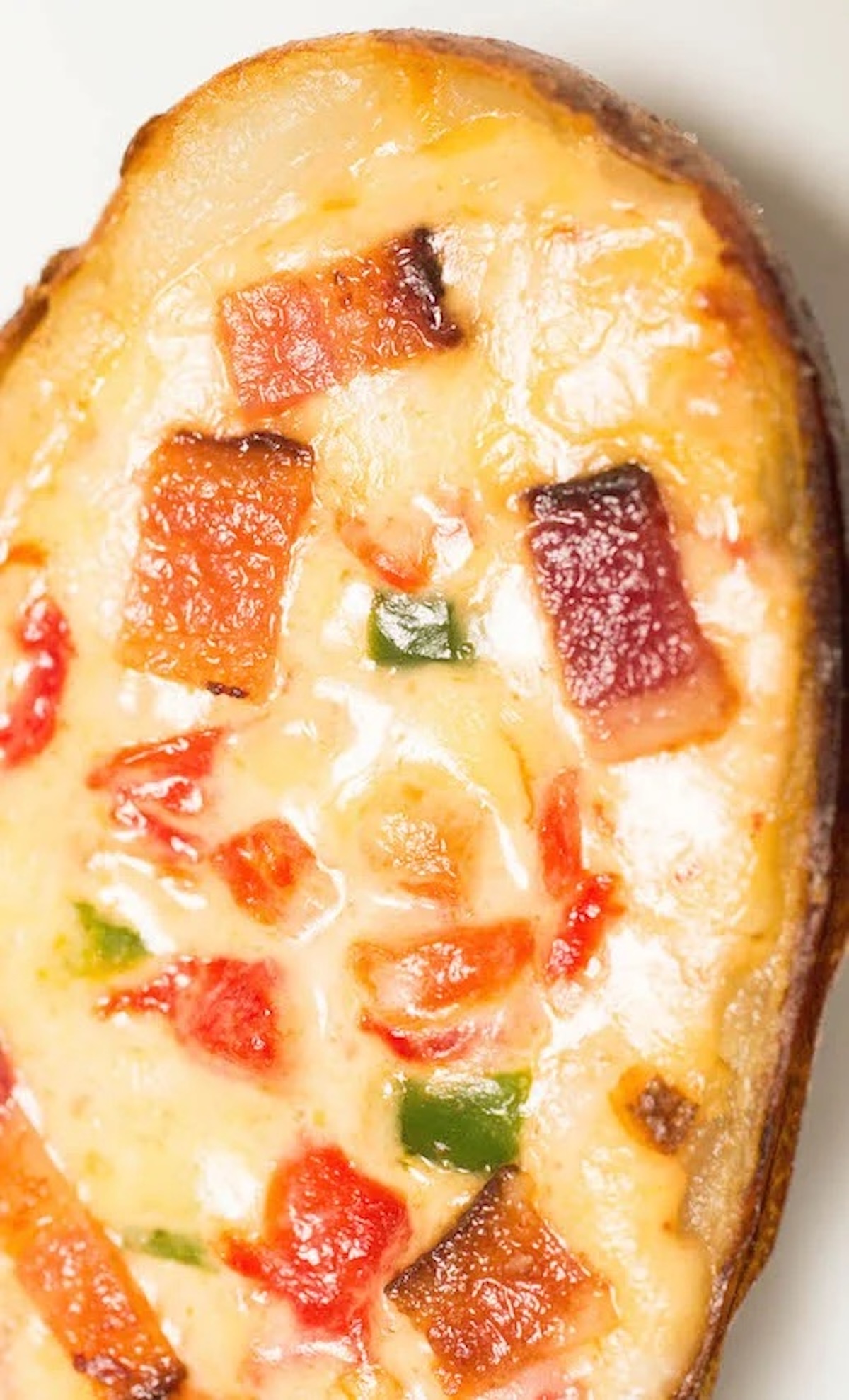 A potato skin filled with melted cheese, large pieces of diced bacon, and diced jalapeño and pimento peppers.