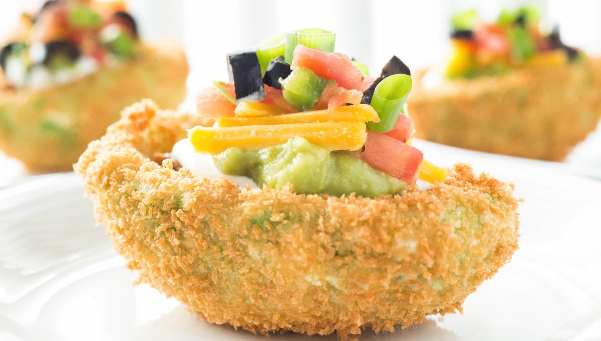 A fried seven layer stuffed avocado is in focus in the foreground, two more are out of focus in the background.