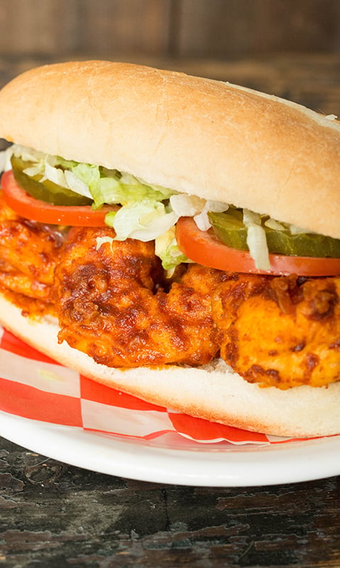 Homemade Nashville Hot Shrimp Po Boy topped with sliced tomato, pickles, and shredded lettuce.