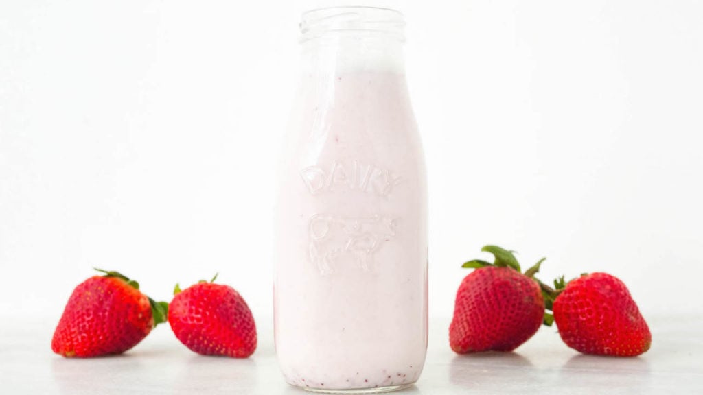 Homemade Strawberry Milk Recipe in a glass milk bottle on a white background. 