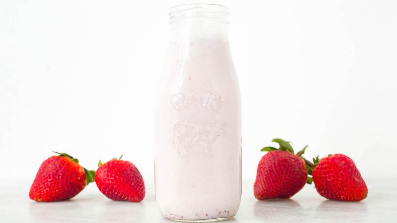 Homemade Strawberry Milk Recipe in a glass milk bottle on a white background. 