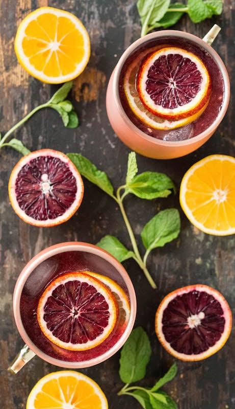 Overhead view of two copper mugs with blood orange & Meyer lemon Moscow mules surrounded by fresh mint and sliced citrus.