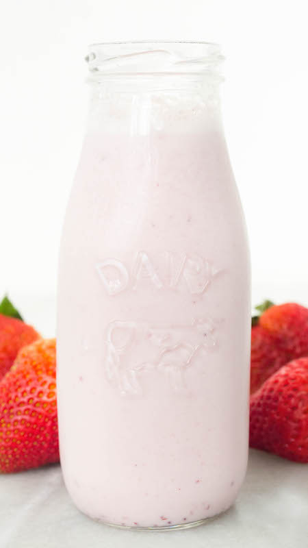Homemade Strawberry Milk Recipe in a glass milk bottle next to fresh strawberries.