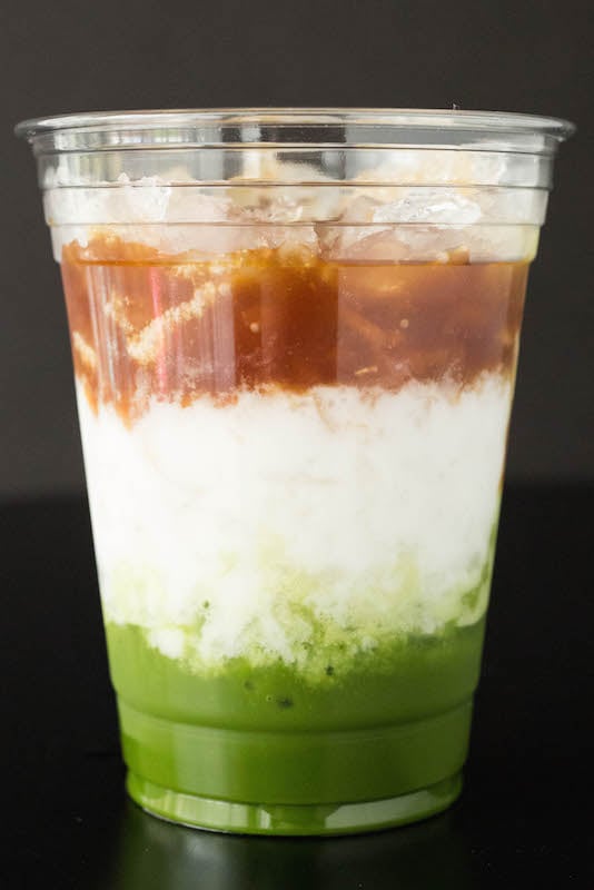 A Starbucks Matcha Espresso Fusion Drink with distinct layers of matcha, milk, and coffee on a black background.