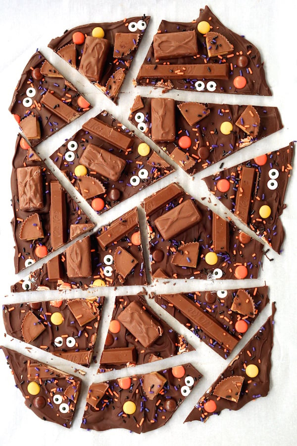 Overhead shot looking down on chocolate bark that's decorated with bite sized candy bars, candy eyes, and black & orange sprinkles