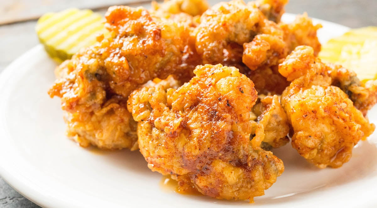 Nashville Hot Fried Oysters on a white plate with pickle slices in the background.