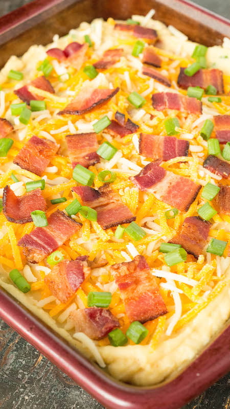 A baking dish with Instant Pot Twice Baked Potato Casserole that has been topped with shredded cheese, cooked pieces of bacon, and green onions.