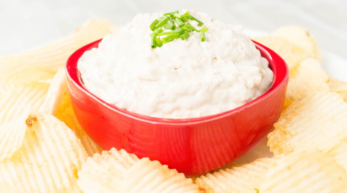 A small red bowl filled with Instant Pot Caramelized Onion Dip surrounded by potato chips.