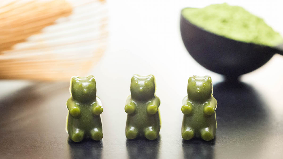 Three Homemade Matcha Gummy Bears in front of a matcha whisk and matcha powder.