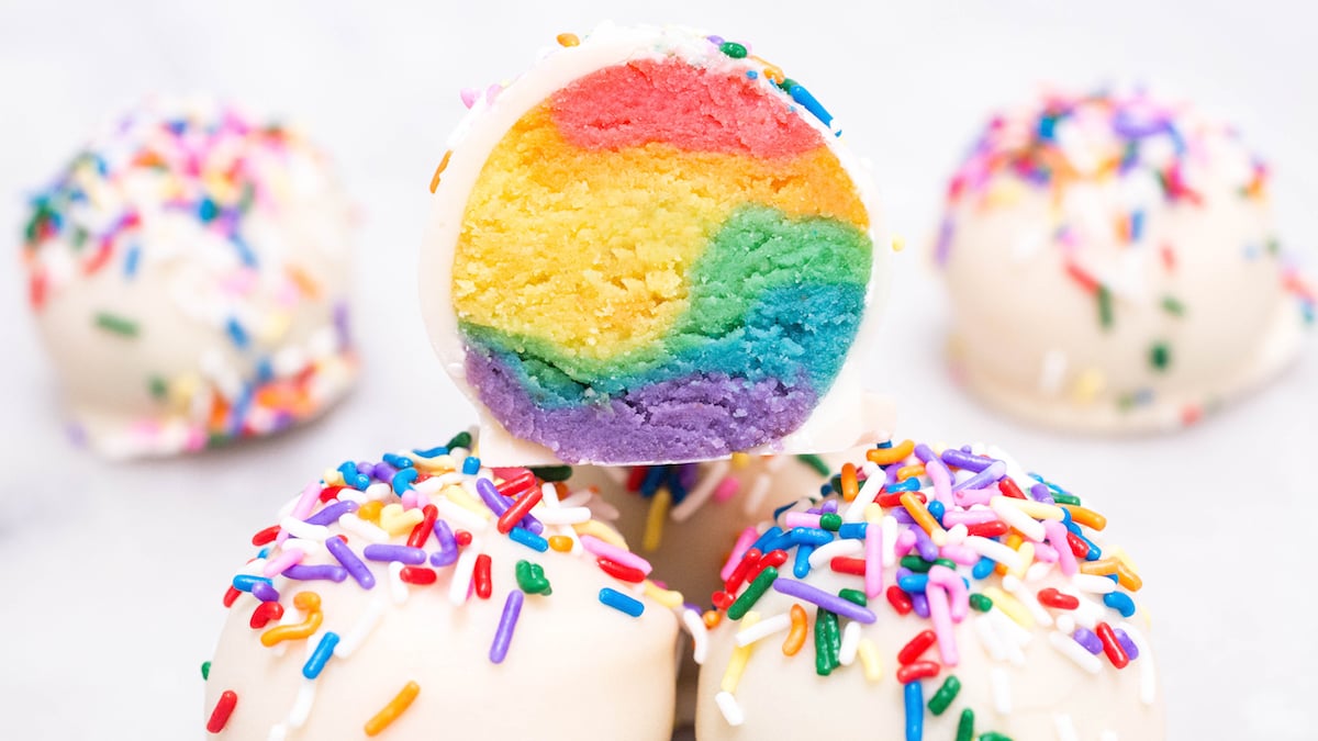 Three Rainbow Cake Truffles stacked on top of each other. One is cut open to show the multi-colored insides.