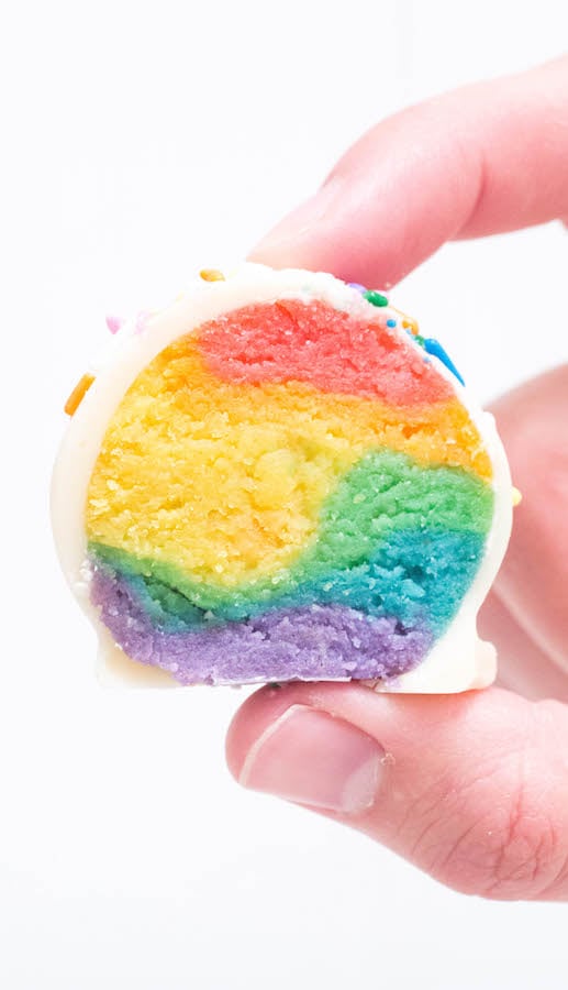 A close up of a hand holding a Rainbow Cake Truffle that has been cut in half.