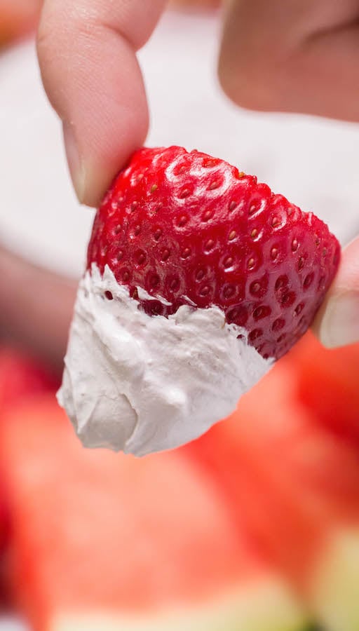 A hand holds up a strawberry that's been dipped in Red Wine Fruit Dip.