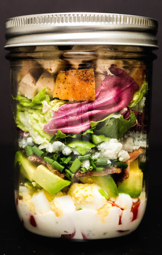 A mason jar filled with Cobb Salad on a black background.