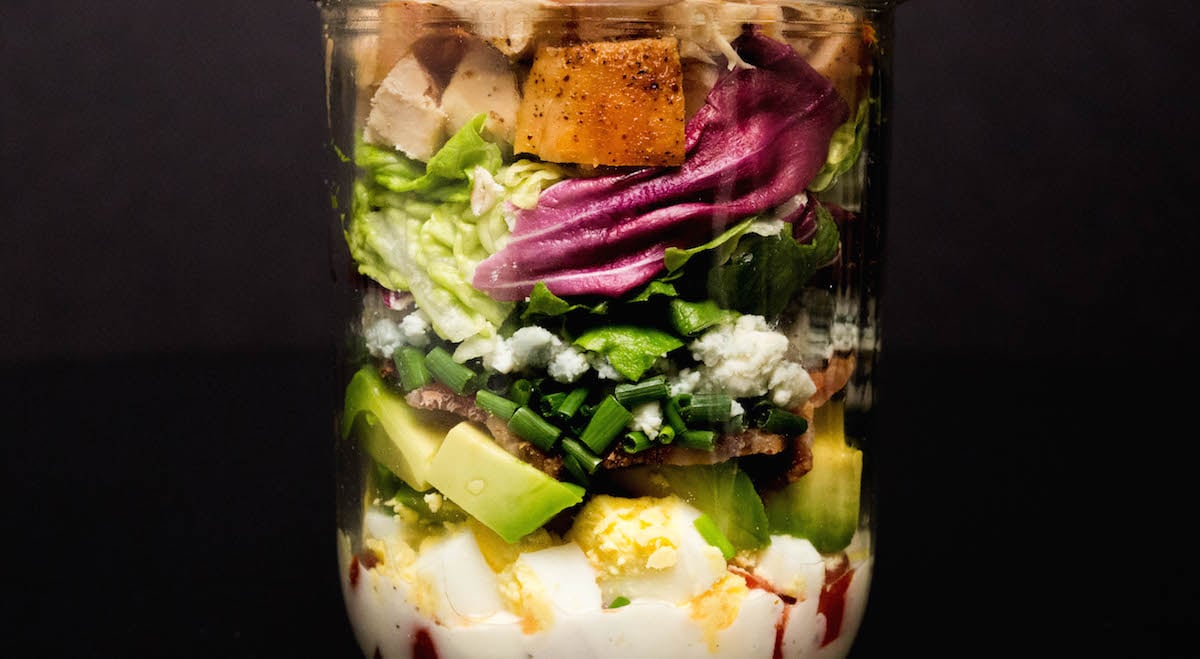 A mason jar filled with Cobb Salad on a black background.