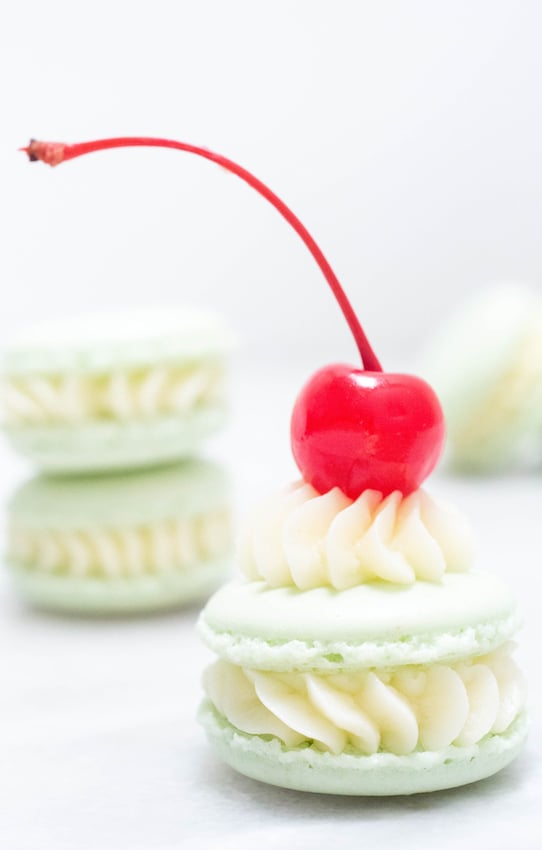 Close up with a Shamrock Shake Macaron with a maraschino cherry on top.