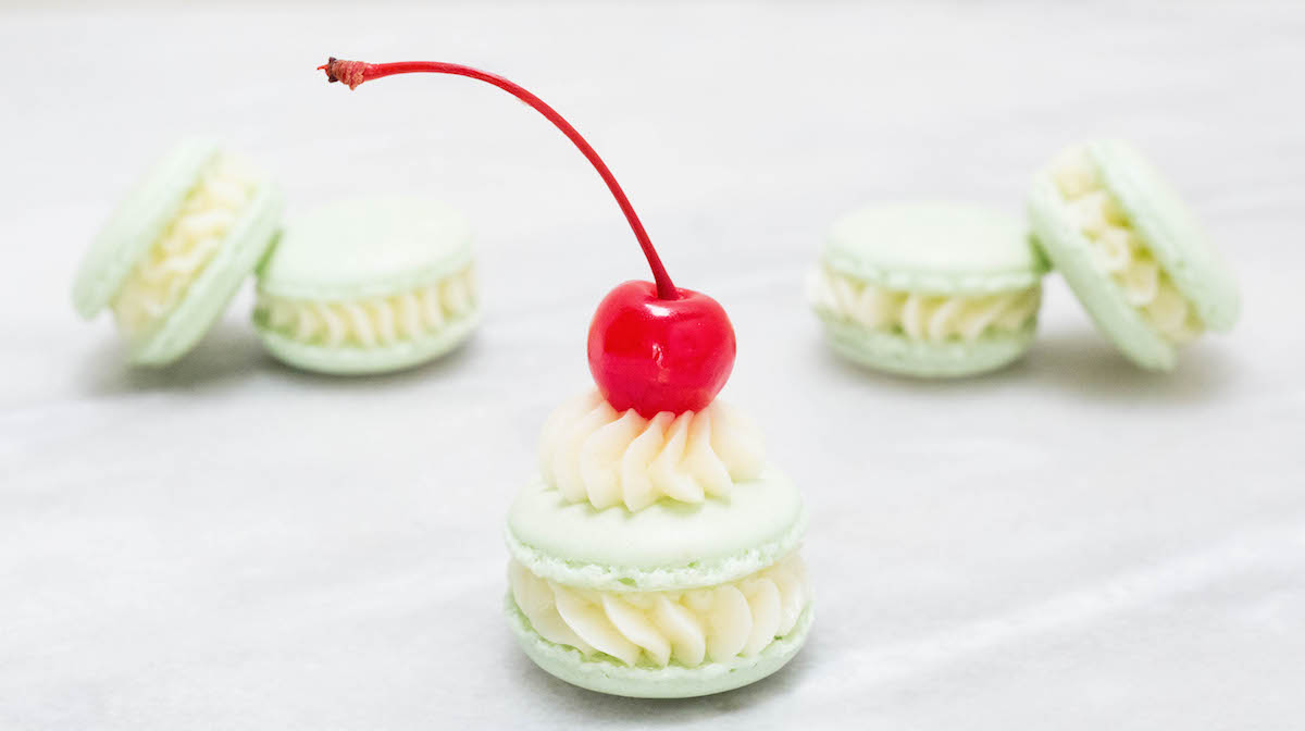 Shamrock Shake Macarons on a white background. The one in front is garnished with a maraschino cherry.